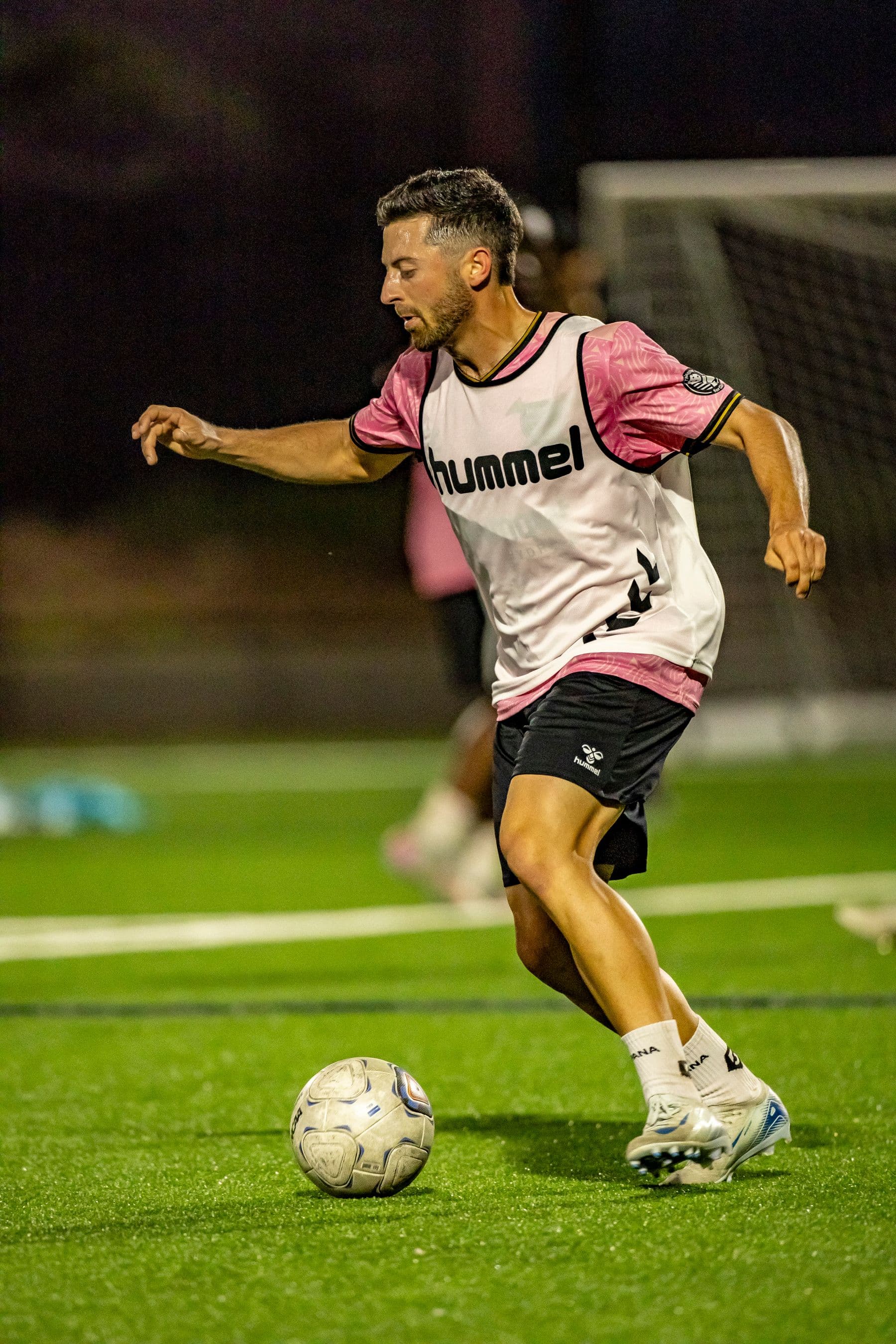 Footballer training with a ball on a floodlit pitch