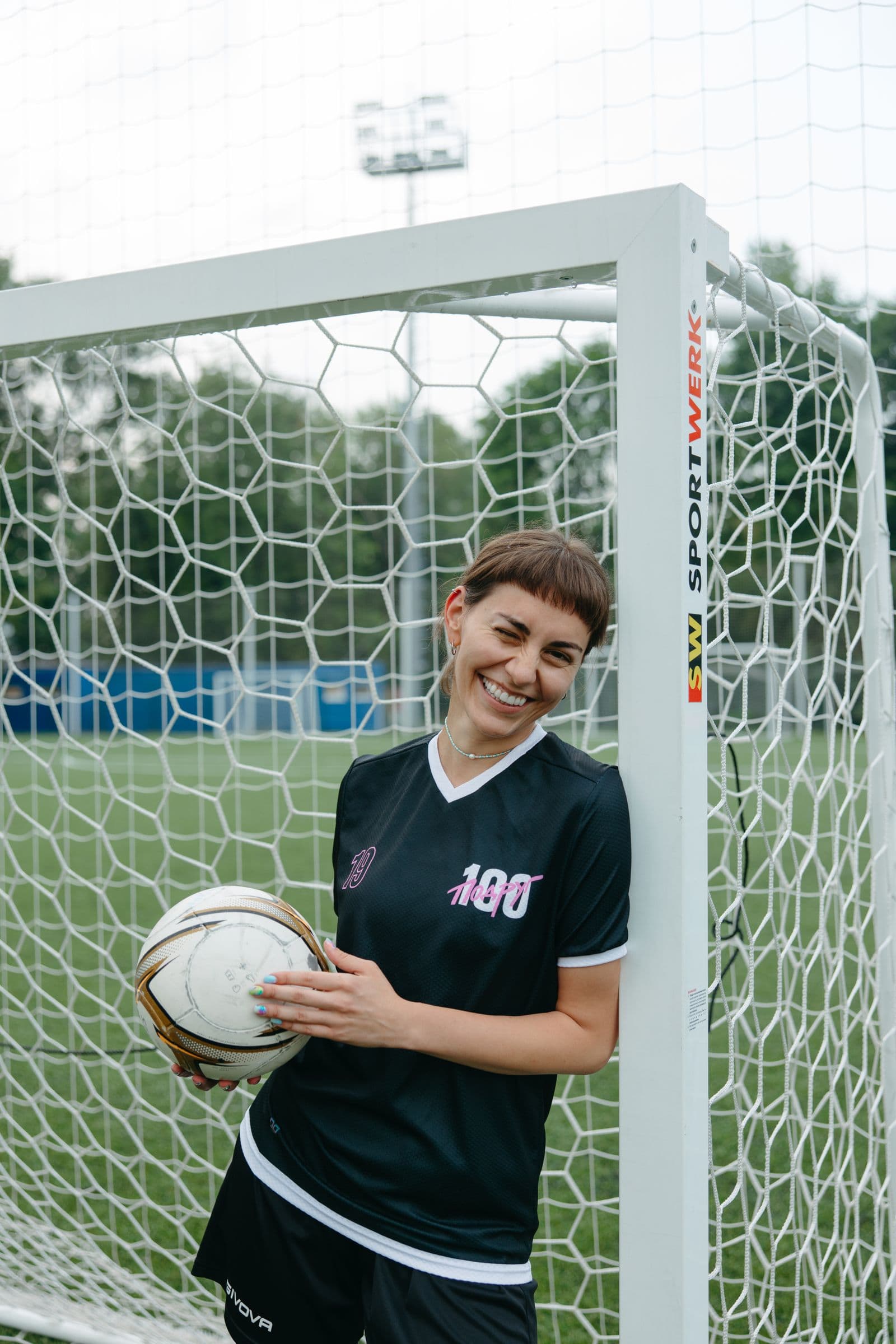 Woman footballer posing with a ball beside a goal